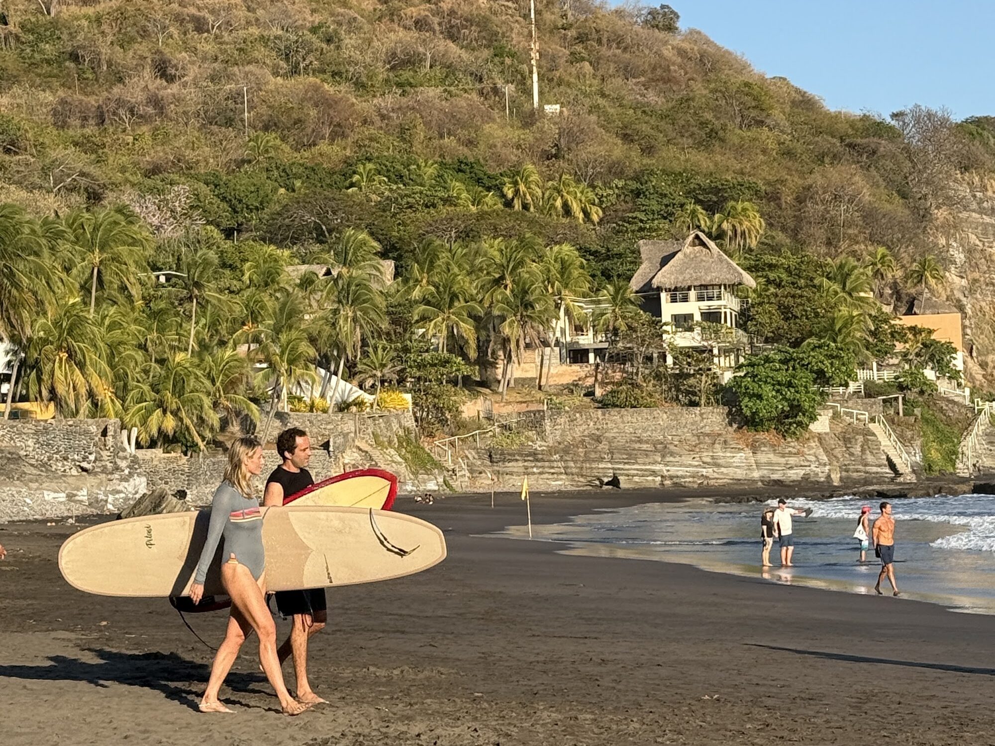 Two surfers walking on a black sand beach on El Salvador's coast